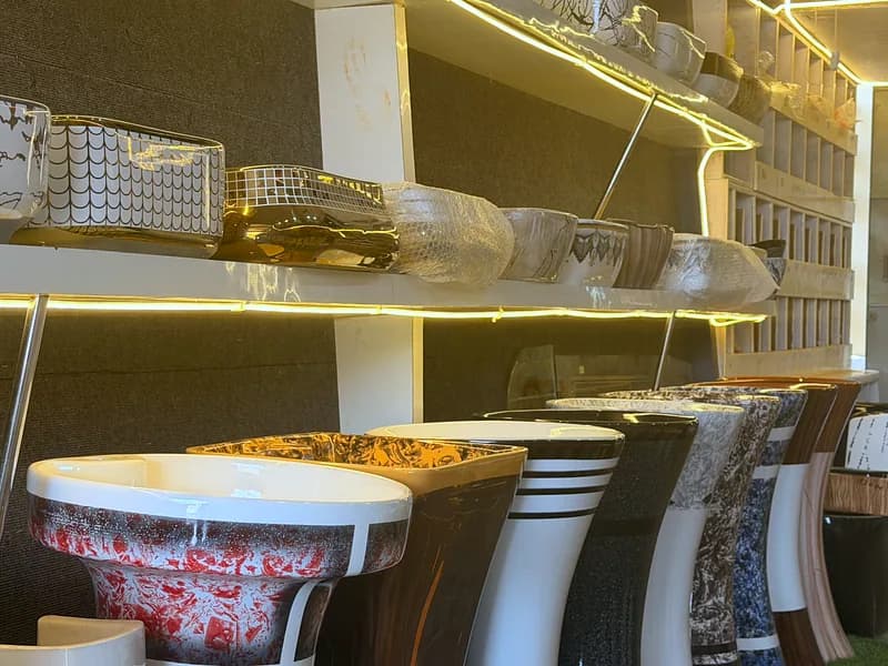 Pedestal wash basins in patterned finishes beside lit display shelves of counter-top basins