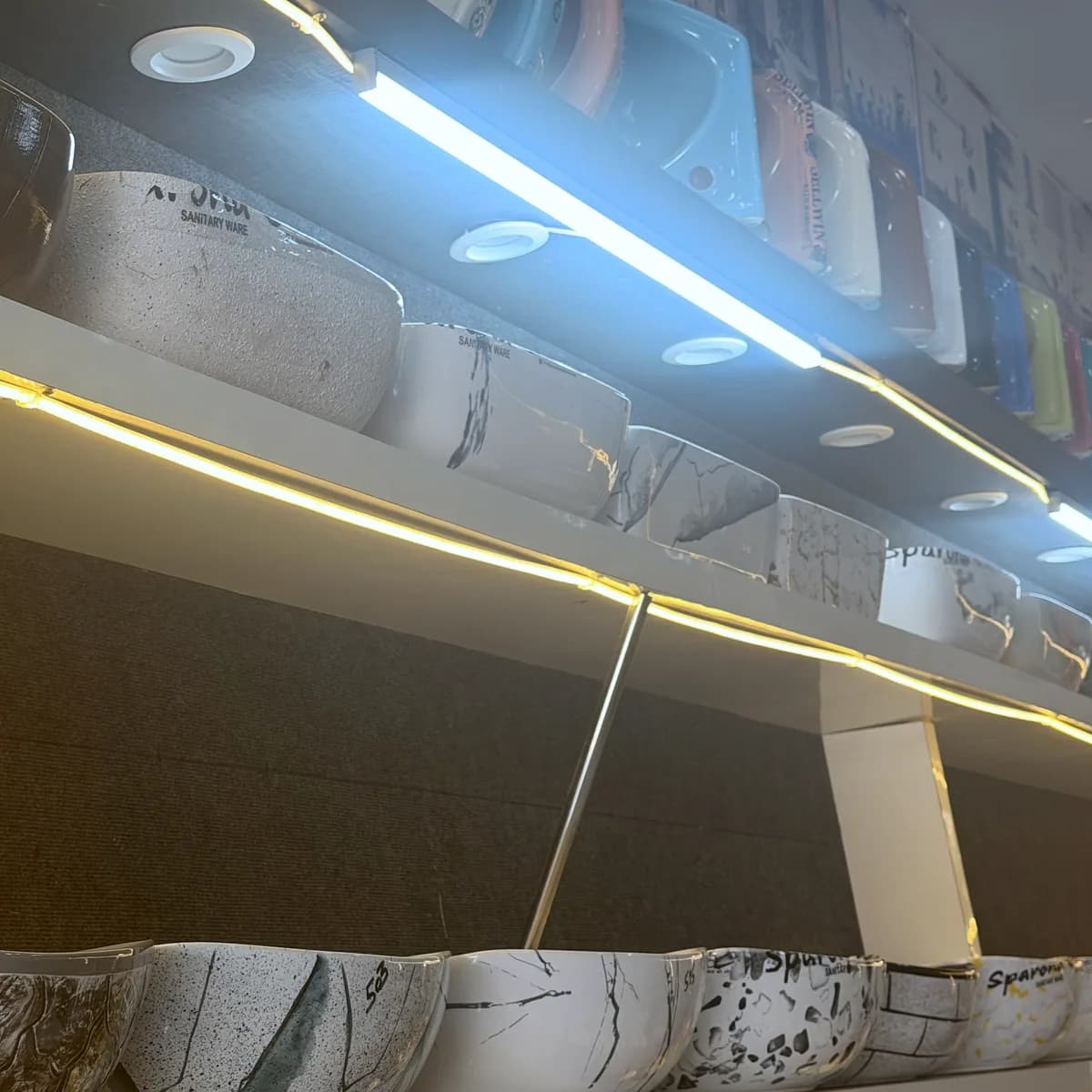 Illuminated display shelves stacked with counter-top basins in many finishes
